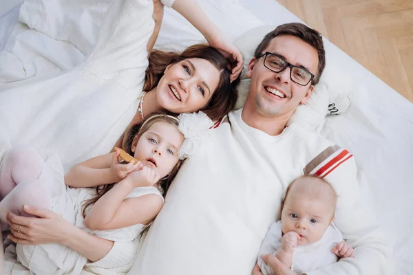 Happy Cheerful caucasian family in neutral clothes together., Mother, Father, daughter and son laying on the bed — Stock Photo, Image