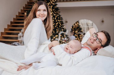 Tarafsız giysiler içinde mutlu beyaz bir aile anne, baba, kız ve oğul yatakta uzanıyorlar. 