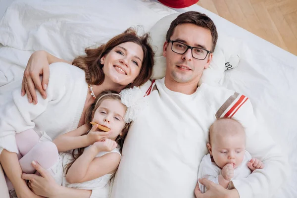 Χαρούμενη χαρούμενη καυκάσια οικογένεια με ουδέτερα ρούχα μαζί., Μητέρα, Πατέρας, κόρη και γιος ξαπλωμένοι στο κρεβάτι — Φωτογραφία Αρχείου