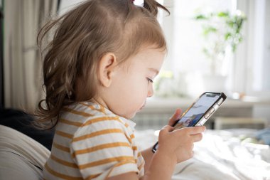 Küçük kız akıllı telefonuyla evde yatağında oynuyordu. Kafkasyalı küçük kız..