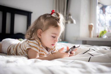Küçük kız akıllı telefonuyla evde yatağında oynuyordu. Kafkasyalı küçük kız..
