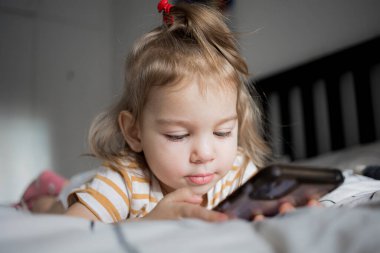 Küçük kız akıllı telefonuyla evde yatağında oynuyordu. Kafkasyalı küçük kız..