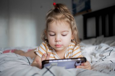 Küçük kız akıllı telefonuyla evde yatağında oynuyordu. Kafkasyalı küçük kız..