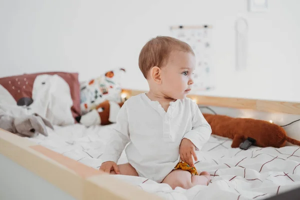 Baby meisje zit op bed in neutrale tinten kinderkamer. Geslacht neutrale babykamer en kleding — Stockfoto