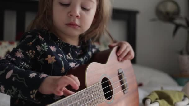 Peuter meisje spelen op ukelele gitaar naar haar pluche speelgoed vriend — Stockvideo