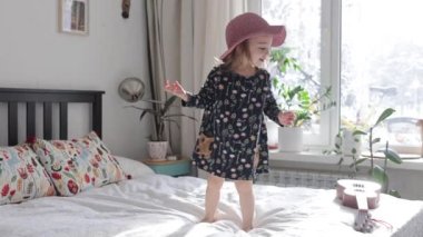 Küçük kız evde ebeveyn yatağında zıplıyor.