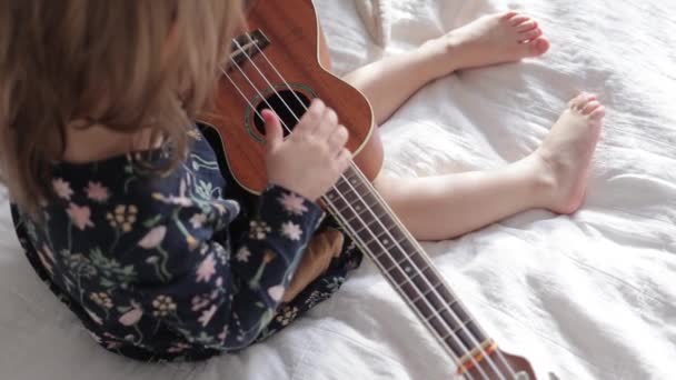 Småbarn flicka som spelar på ukulele gitarr till sin plysch leksak vän — Stockvideo