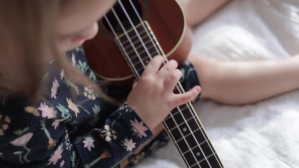蹒跚学步的女孩用ukulele吉他弹奏给她的毛绒玩具朋友 — 图库视频影像