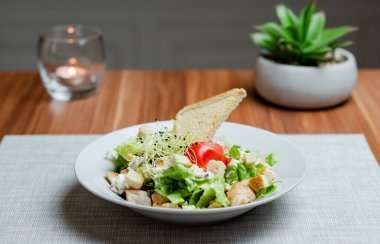Caesar Salad with chicken breast, lettuce and toast on wooden table, inside hotel. High quality photo