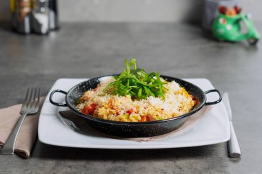 Risotto with vegetables and roasted chicken breast in the black metal pot on top with Arugula. High quality photo