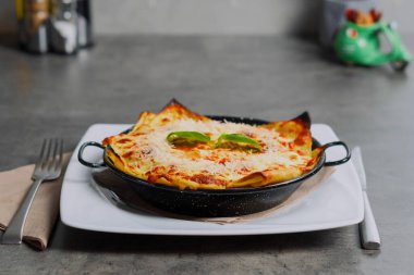 Close-up of a traditional lasagna made with minced beef bolognese sauce topped with basil leafs served on a white plate. High quality photo