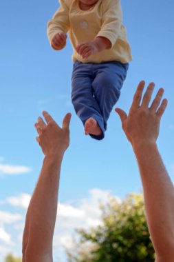 The child is thrown by the father's arms against the blue sky