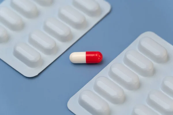 One Red and White Capsule Vitamin supplement in between two blister packs of medication on Blue background