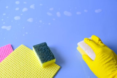 Sarı lastik eldivenli el mavi arka planda temizlik süngeri tutuyor..