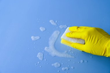 Sarı lastik eldivenli el mavi arka planda temizlik süngeri tutuyor..