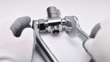 İngiliz anahtarı olan bir tesisatçı beyaz arka plandaki musluğu tamir ediyor. Bir saptırıcının onarımı ve bakımı. Yönlendirici, suyun borudan geçmesini sağlayan bir anahtardır..