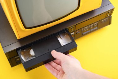 VHS video kasedi videoyu izlemek için kayıt cihazına konur. 1980 'lerden, 1990' lardan, 2000 'lerden siyah arkaplanda video kaseti olan eski sarı renkli televizyon.. 