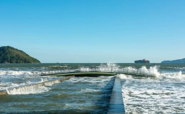 City of Santos, Brazil. High tide invades a strip of sand on the beach. Lighthouse and water channel number 6 and bridge.