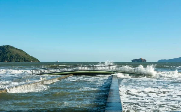 City of Santos, Brazil. High tide invades a strip of sand on the beach. Lighthouse and water channel number 6 and bridge.