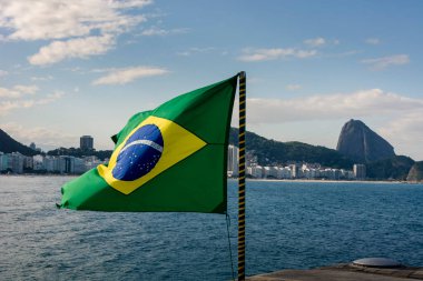 Rio de Janeiro, Brazil. Brazil flag fluttering with Copacabana waterfront and Sugar Loaf in the background on a sunny day.