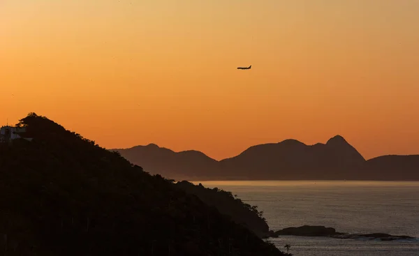 Airplane flying over the mountains at sunrise. Silhouettes and various shades of yellow and orange. Guanabara bay, Rio de Janeiro, Brazil. 