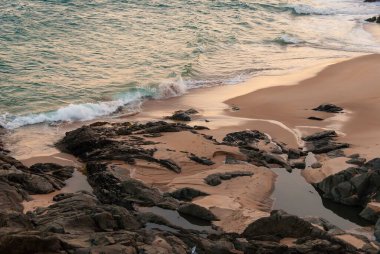 Beach in the late afternoon of summer. Turquoise sea and waves, rocks and sand. Rio Vermelho, Salvador, Brazil