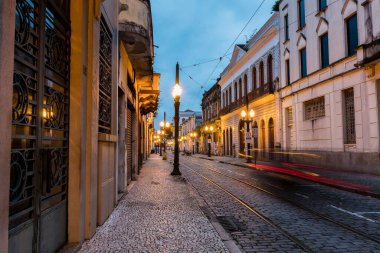 Old center of the city of Santos, Brazil. Street of Trade. Stone street, facades of old houses, old cast iron poles with yellow light and in the background the church of Valongo