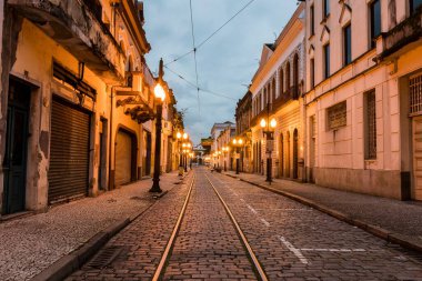 Santos, Sao Paulo, Brazil. Historic center, Comercio Street in the early evening illuminated with yellow lights, cast iron poles and stone floor. In the background, Valongo church.