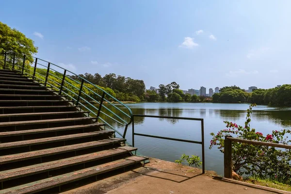 Ibirapuera Park, Sao Paulo, Brazil. Bridge over the lake with a view of the park and the city buildings in the background on a sunny afternoon with blue sky.