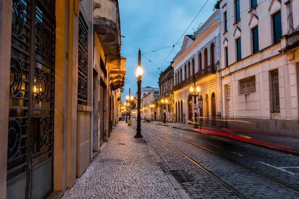 Old center of the city of Santos, Brazil. Street of Trade. Stone street, facades of old houses, old cast iron poles with yellow light and in the background the church of Valongo