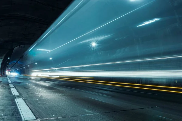 Trails of car lights passing fast through the highway tunnel in perspective.