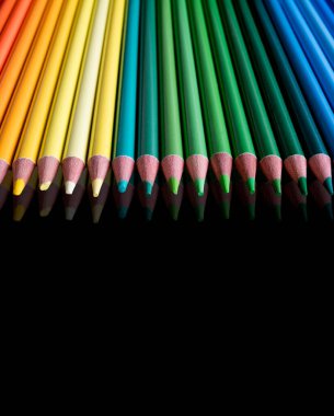 Several colored pencils in perspective arranged gradually. Orange, yellow, green and blue. Black background