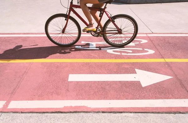 Bike path. Partial view of the tanned legs of a woman wearing yellow slippers and pedaling her red bicycle along the cycle path properly signposted with a bicycle symbol and arrow indicating direction