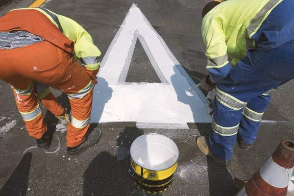 Traffic signage. Asphalt painting. Workers painting the floor. Preference sign at the intersection.