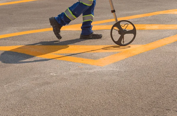 Yeni boyanmış sarı şeritleri ölçüyorum. İşçi ve trafik işareti.
