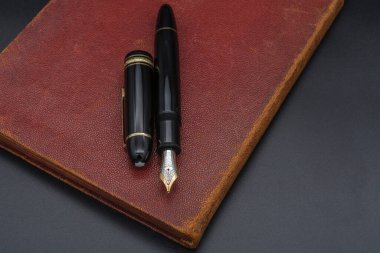 Montblanc Meister eski ve yıpranmış kırmızı bir kitaba 149 dolmakalem yapıştırdı. Siyah arka plan. Santos, SP - Brezilya, 27 Kasım 2020.