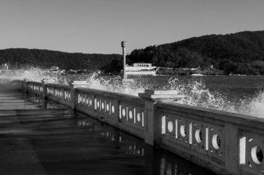 Santos, Brezilya. Dalgalar plaj duvarına vuruyor, Portekiz standart tarihi anıtı ve liman kanalındaki Barra kalesine vuruyor. Siyah ve beyaz resim. 