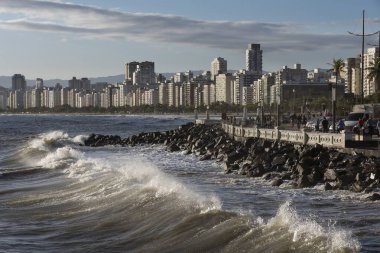 Dalgalar dalgalar yükseldiğinde kıyıya yaklaşıyor. Brezilya 'nın Santos kentindeki sahil duvarı ve liman binaları.
