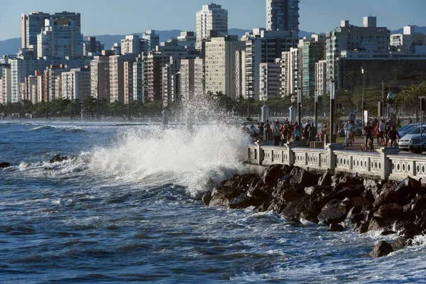 Santos, Brezilya. Yüksek kış gelgitleri sırasında dalgalar kıyıya çarpar. Sahil duvarı ve rıhtım binaları. Ponta da Praia bölgesinde insanlar kaldırımda yürüyor.