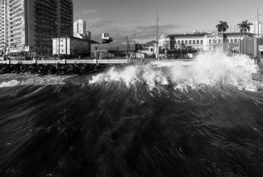 Santos şehri, Brezilya. Kış mevsiminde dalgalar kıyıya vurur. Ponta da Praia bölgesindeki sahil ve deniz kenarı binaları. 23 Eylül 2022. Siyah ve beyaz resim. 