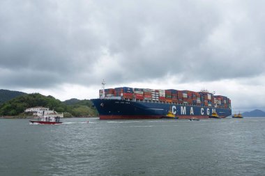 Santos şehri, Brezilya. Konteyner gemisi CMA CGM Yelkenlisi bulutlu bir günde liman kanalına girdi. Arka planda, Barra Kalesi. 24 Ekim 2022. 