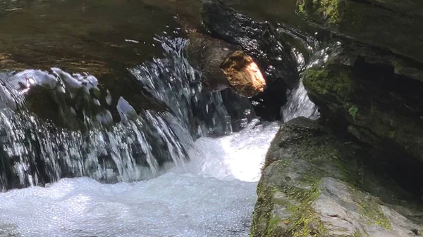 water flowing over rocks on the river forming bubbles with mossy rocks