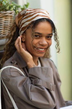 portrait of joyful african american woman in headscarf and stylish trench coat on street in prague 