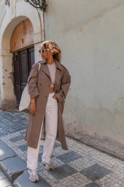 full length of stylish african american woman in headscarf and sunglasses posing with reusable bag on street in prague 