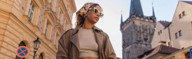 stylish african american woman posing near old town hall tower in prague, banner
