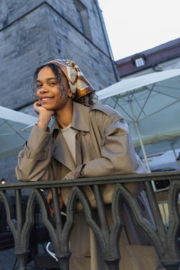 cheerful african american woman in stylish outfit and headscarf smiling on street in prague 