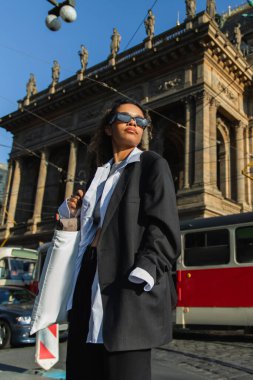 low angle view of young african american woman in sunglasses posing near national theatre in prague