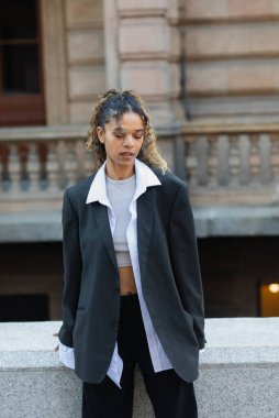 young african american woman in oversize suit standing on urban street in prague