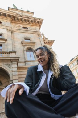 low angle view of happy african american woman listening music in wireless earphone near national theatre in prague 