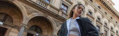 low angle view of african american woman in wireless earphone posing near building of national theater in prague, banner